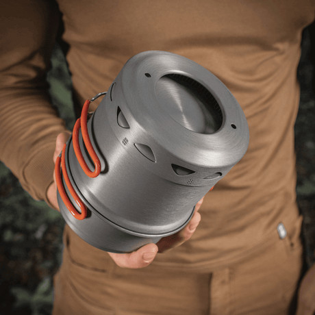Person som håller ett M-Tac Individuellt kokset för brännare i anodiserad aluminium, lämpligt för camping och friluftsliv.