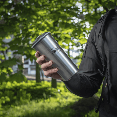 Person håller en M-Tac Termokopp 450 ml med ventil i en grön skog.
