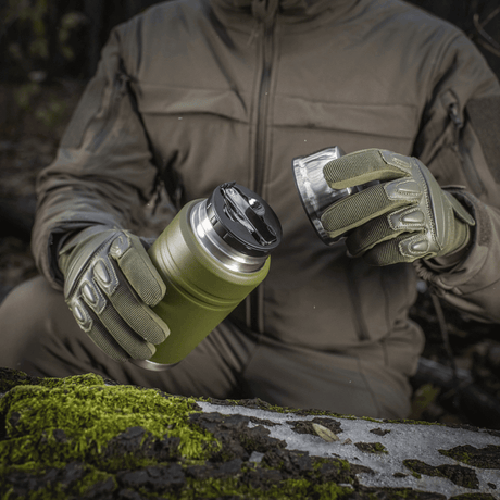 Friluftssituation med M-Tac termosflaska 750 ml med hopfällbar sked i handskar, idealisk för camping och utflykter.