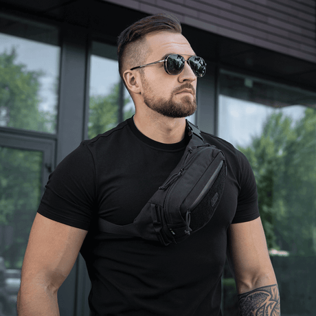 Man bär M-Tac Bältesväska Gen.II i svart, designad med funktionell stil, bärs över axeln.