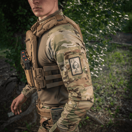 Man i kamouflage med M-Tac Patch Ace of Spades på armen i naturmiljö.