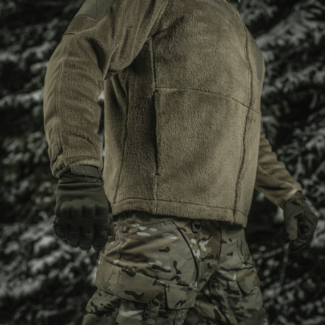 Militærperson iført M-Tac Battle Fleece Polartec Jakke i skovområde, viser funktion og pasform af jakken.