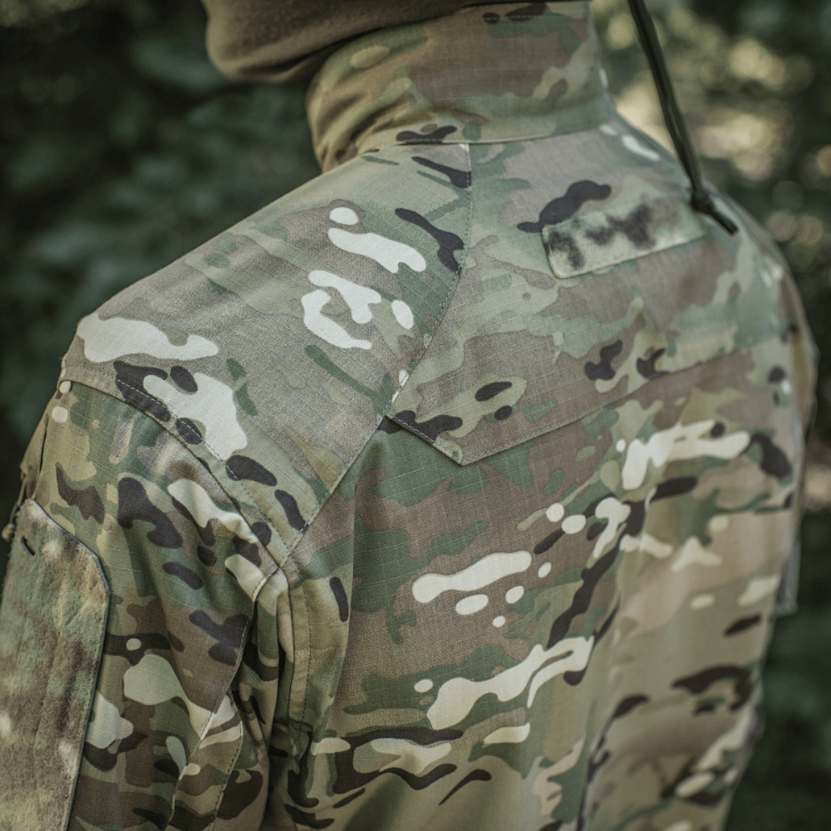 M-Tac Jakke Sturm Gen.II NYCO Extreme i Multicam camouflage-design med NIR-teknologi, set bagfra i udendørs miljø.