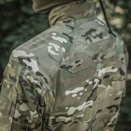 M-Tac Jakke Sturm Gen.II NYCO Extreme i Multicam camouflage-design med NIR-teknologi, set bagfra i udendørs miljø.