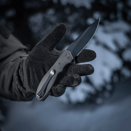 M-Tac Outdoor & Militär fällkniv - Type 6 i snöklädd miljö, hålls av en svarthandskad hand.