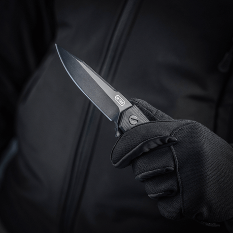 M-Tac Outdoor & Militär fällkniv - Type 6 hålls i en hand med svart handske, kromat rostfritt stålblad, G10-komposithandtag.