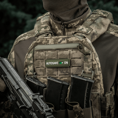 Soldat bär militärväst med M-Tac Patch Autosave PVC med 3D-effekt, velcro och fullfärg för taktisk användning.