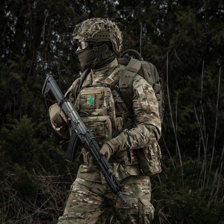 Soldat i militäruniform med M-Tac Patch Lucky Card (Broderi) fäst på västen, symbol för tur och skydd, kamouflage i skogsområde.