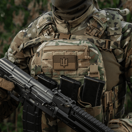 Soldat i camouflageväst med M-Tac patch Ukraine Flag med ZSU Trident PVC, håller gevär, symboliserar ukrainsk stolthet och arv