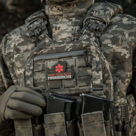 Taktisk väst med påsatt patch, "Odin Vils Make Paramedicine", i kamouflagemönster.