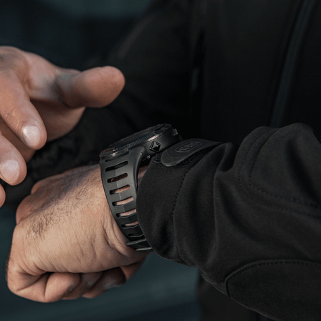 Person justerar M-Tac Tactical Ur 2147 på handleden. Idealisk för utomhus och taktisk användning med robust design och praktiska funktioner.
