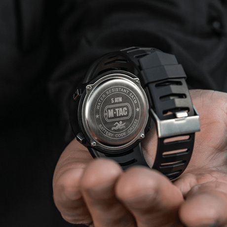 M-Tac Tactical Ur 2147 med stållock, "WATER RESISTANT 5ATM" och "BATTERY CODE CR2032" visas i en hand.