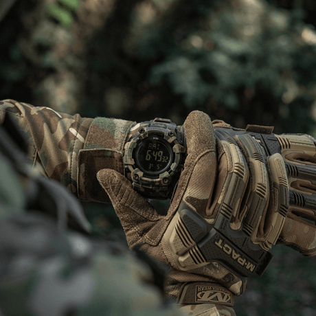M-Tac Tactical Ur 2037 i bruk i naturen, visas på handleden av en person i camouflagekläder, visar LED-bakgrundsbelyst skärm och funktioner.