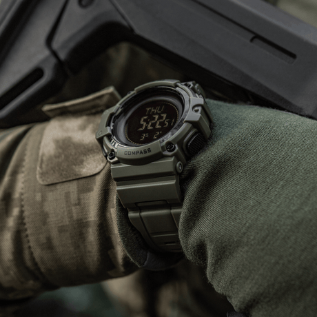 M-Tac Tactical Klocka med Kompass 2233 på militärklädd arm, för utforskning och friluftsäventyr, robust klocka designad för taktisk användning med kompass och LED-display.