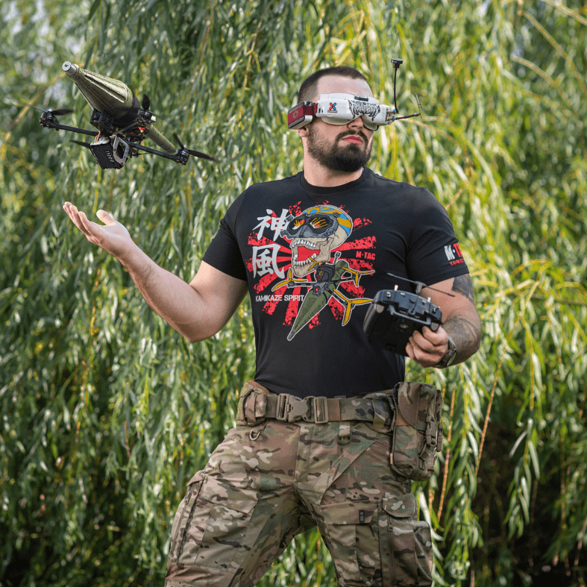 Mand iført M-Tac T-Shirt Kamikaze Spirit med FPV-briller og drone i skovmiljø.