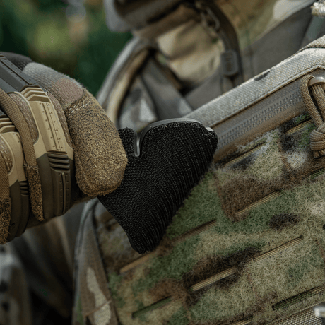 Taktisk handske justerar svart velcro-patch på kamouflagedräkt utomhus.