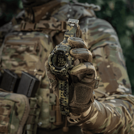 M-Tac Tactical Klocka 2037 i kamouflage, bärs av person i taktisk klädsel, visar tid och datum, idealisk för friluftsliv och vardag.