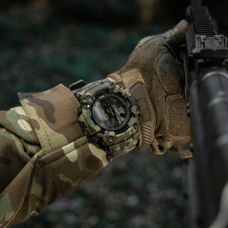 M-Tac Tactical Ur 2037 på handleden med camouflagekläder, idealisk för utomhus och taktisk användning, framhäver robust design och funktionalitet.