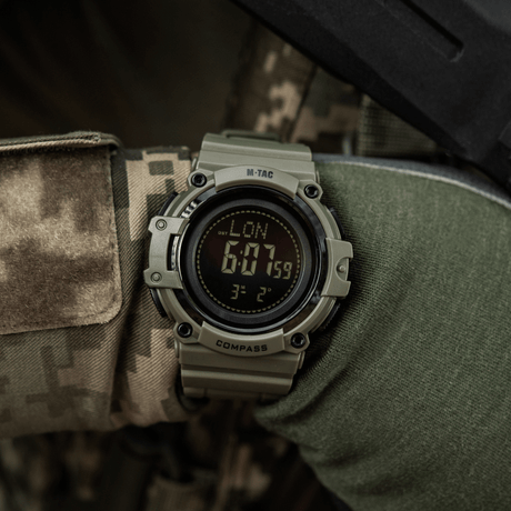 M-Tac Tactical Ur med Kompas 2233 bärs av en person i camouflage, lämplig för utomhusaktiviteter med LED-belysning och stoppur.