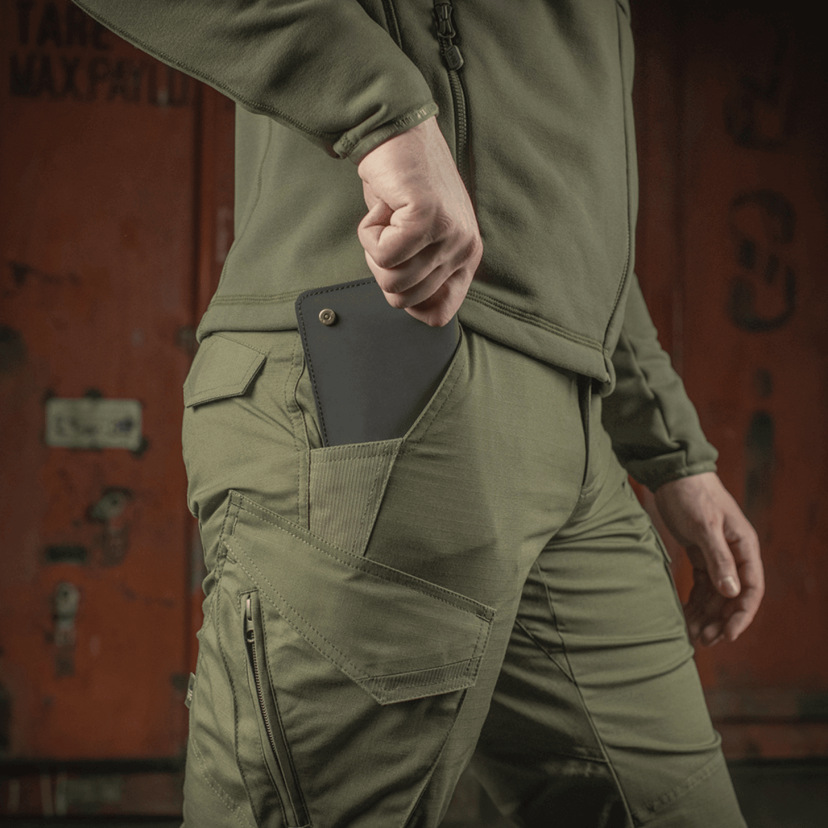 Mand iført M-Tac Taktiske Bukser Aggressor Gen. II Flex med telefon i lommen, fremhæver funktionel design og holdbart stof.
