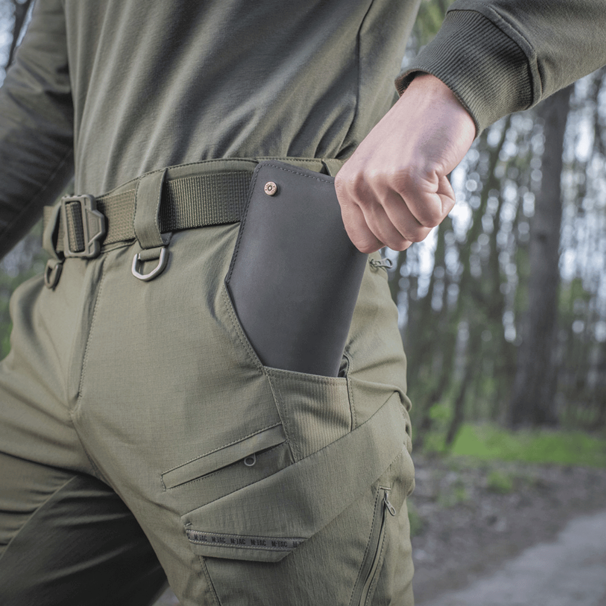 Person iført M-Tac Bukser Aggressor Summer Flex med telefon i lommen på udendørs sti.