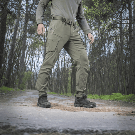 Person iført M-Tac Bukser Aggressor Summer Flex i skov, lette rip-stop nylonstoffer, ideel til varmt vejr og udendørs aktiviteter.