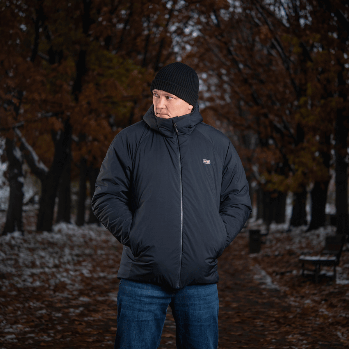 Mand iført en sort M-Tac Paladin Jakke, perfekt til hverdagsbrug, står i en park på en kølig efterårsdag.