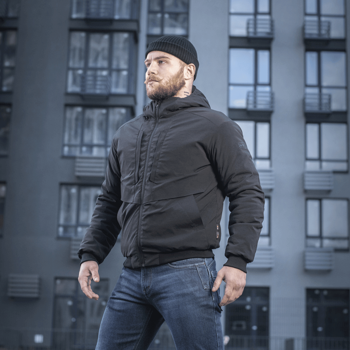 Mand iført M-Tac Rubicon Jakke Gen. II – Slidstærk og varm bomberjakke foran moderne bygning