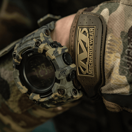 M-Tac Tactical Ur 2037 med robust design, perfekt för utomhus och taktiska aktiviteter, visad på camouflagedräkt mot en naturfärgad bakgrund.