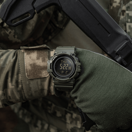 M-Tac Tactical Ur med Kompas 2233 fäst vid taktisk utrustning som används av en person, lämplig för utomhus- och taktisk användning, med LED-bakgrundsbelysning.