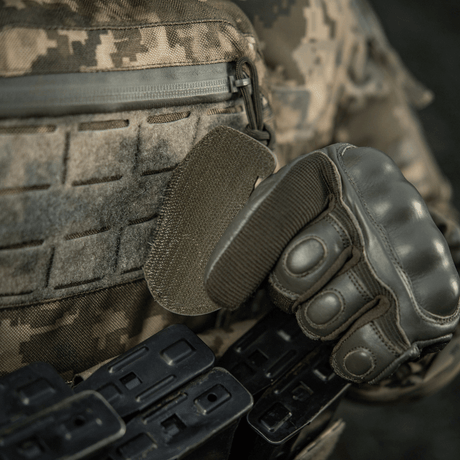 Soldat i taktisk utrustning och handskar fäster M-Tac Patch M67 granat 3D PVC med Velcro-baksida på kamouflerad uniform.