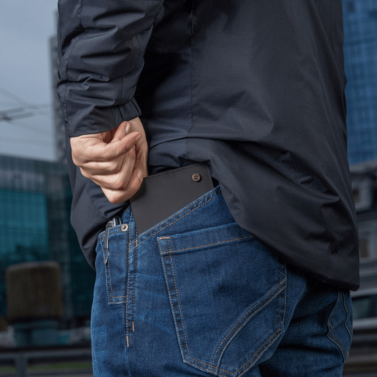 Person placerer M‑Tac Pung Slim Elite i baglommen på jeans.