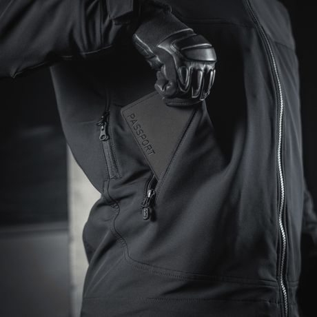 Person i sort jakke holder M‑Tac Pascover med "Passport"-tryk.