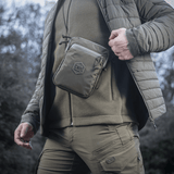 Person wearing the M‑Tac Pocket Bag Elite HEX in a rugged outdoor setting, showcasing its portability and durability.