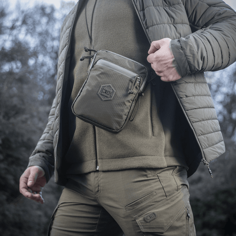 Person wearing the M‑Tac Pocket Bag Elite HEX in a rugged outdoor setting, showcasing its portability and durability.