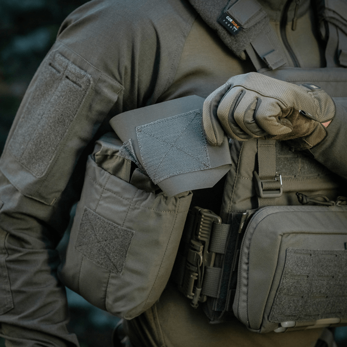 Soldat bruger M‑Tac Medic Pouch Vertical Large Elite til nem adgang til førstehjælpsudstyr, lavet af holdbart Cordura 500D materiale.