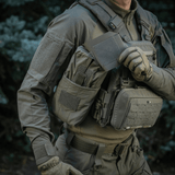 Person wearing tactical gear and holding M‑Tac Medic Pouch Vertical Large Elite in a forest setting.