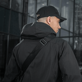 Person carrying M-Tac Tablet Bag Laser Cut Hex over the shoulder with black jacket and cap, urban background.
