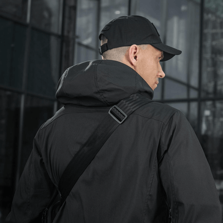 Person carrying M-Tac Tablet Bag Laser Cut Hex over the shoulder with black jacket and cap, urban background.