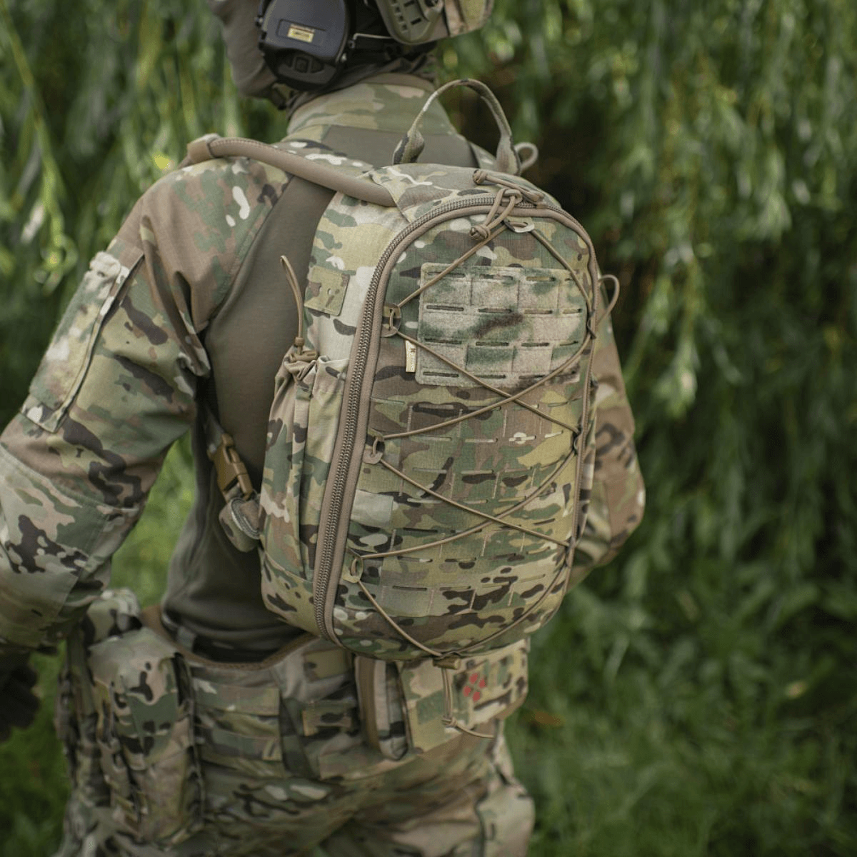 Soldat i camouflageuniform bærer taktisk rygsæk i skovområde