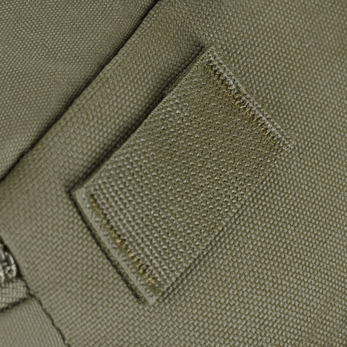 Detalje af olivengrøn tekstil med syning og lynlås på tættet hold