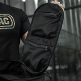 Sort taske med netlommer og lynlåse åbnet på en moderne bybaggrund, betonet af en person i sort trøje.