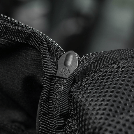 Nærbillede af sort lynlås på rygsæk med netdetaljer, der viser YKK-mærket, fokus på holdbarhed og kvalitet.