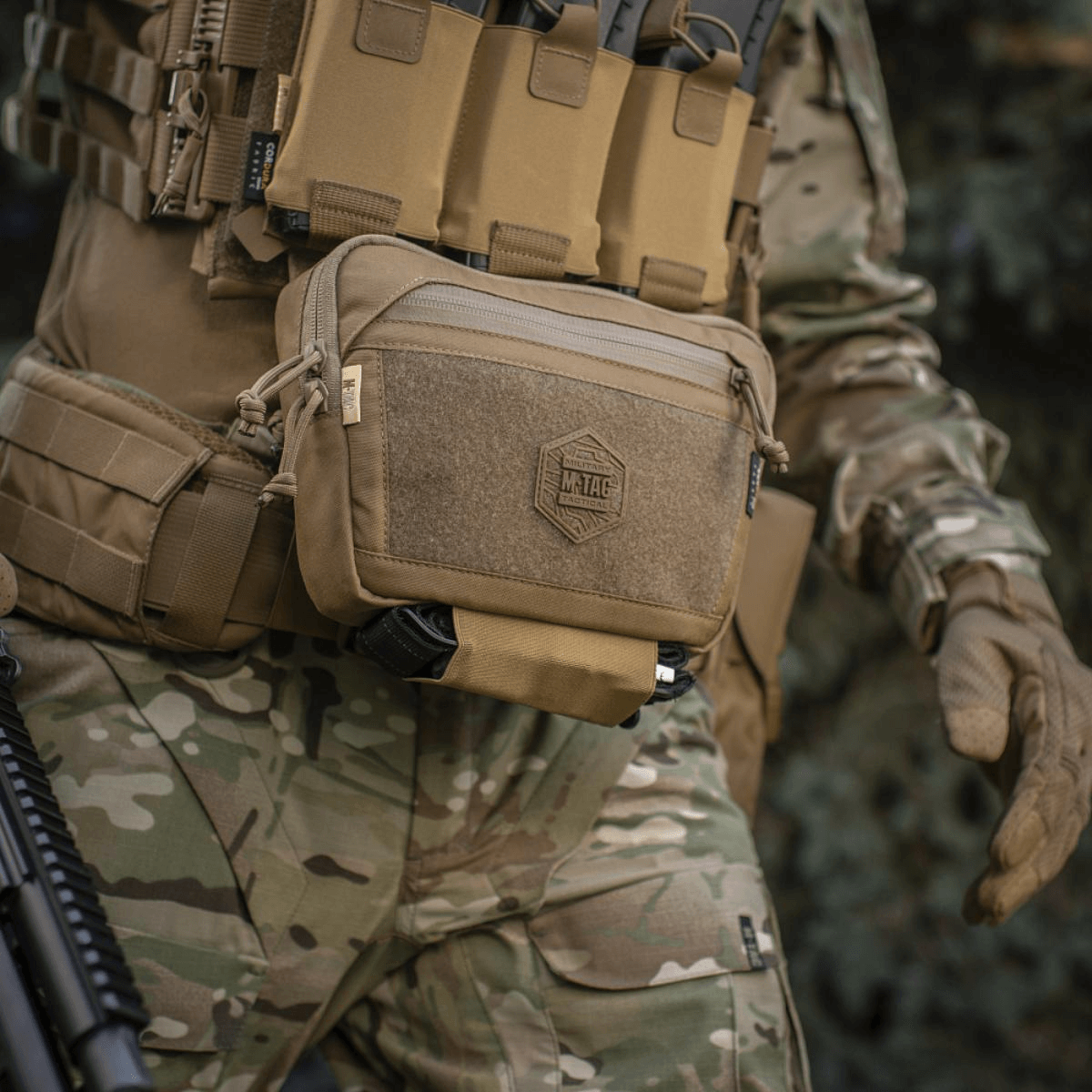 M-Tac Large Elite Gen.II Skuldertaske i brug til taktisk udstyr med Cordura 500D materiale og YKK lynlåse, set i kamouflage omgivelser.