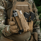 Taktisk udstyr med M‑Tac Tourniquet Pouch Elastic Gen.5 monteret på vest, holdende en tourniquet i naturmiljø på en soldat.