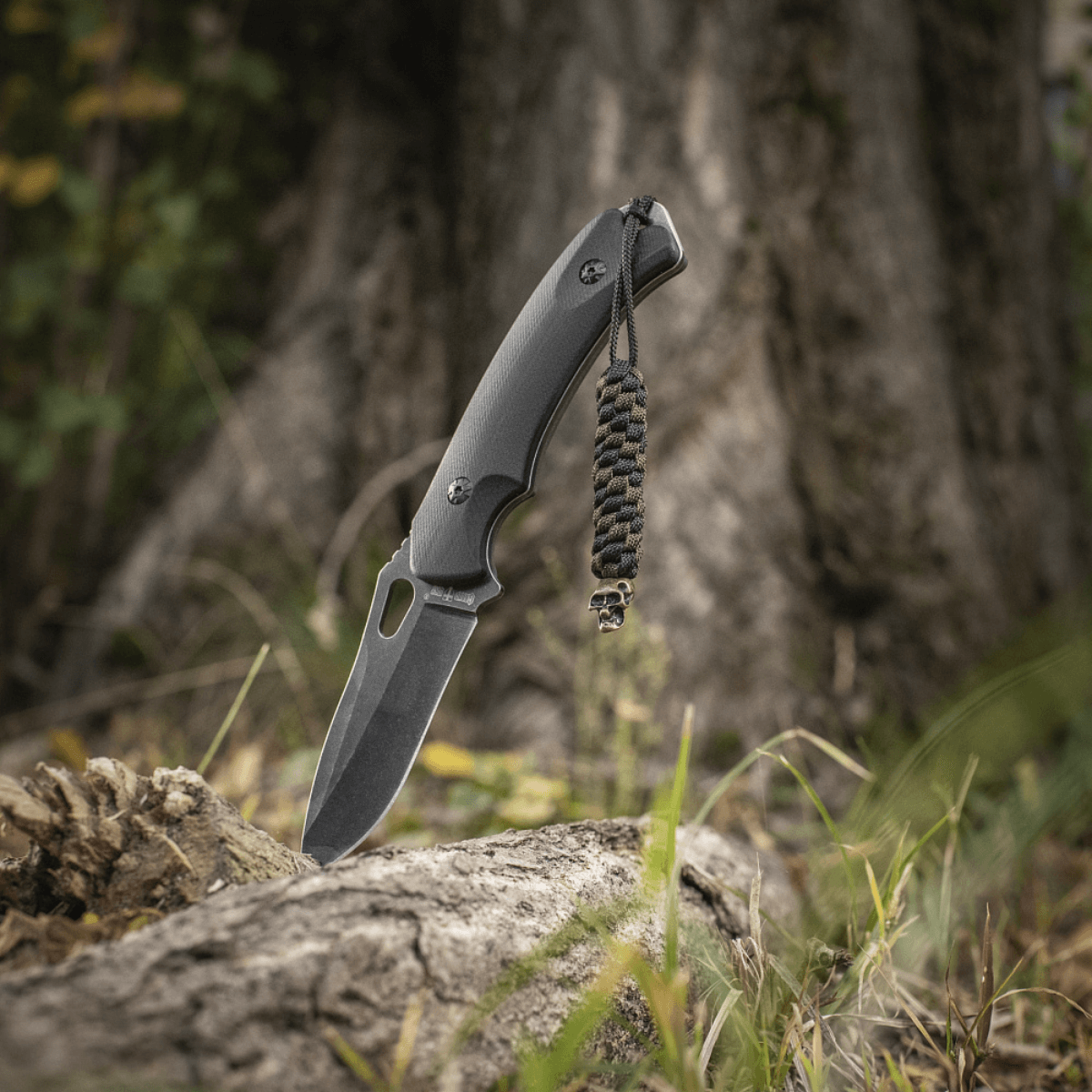 M-Tac Knife Lanyard Helix Skull i flettet paracord på sort kniv mod skovbund