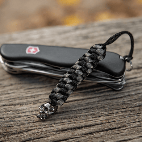 M-Tac Knife Lanyard Helix Skull vedhæftet til en lommekniv, der viser unik stil med flettet paracord og dødningehoveddetalje.