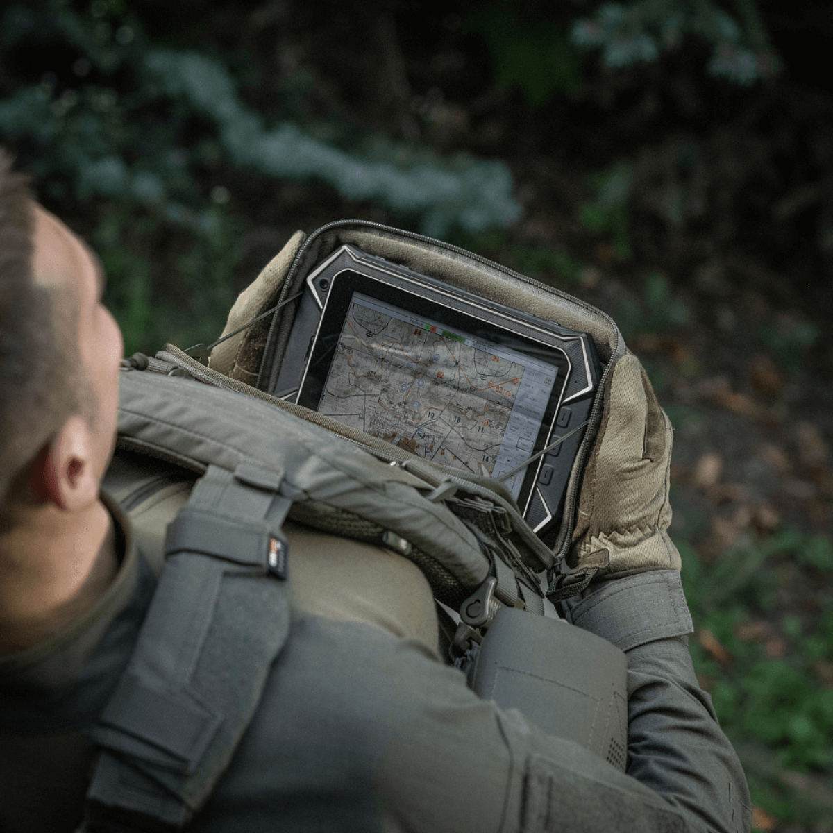 Person med M-Tac Admin Pouch Large Elite holder en tablet i en skov.