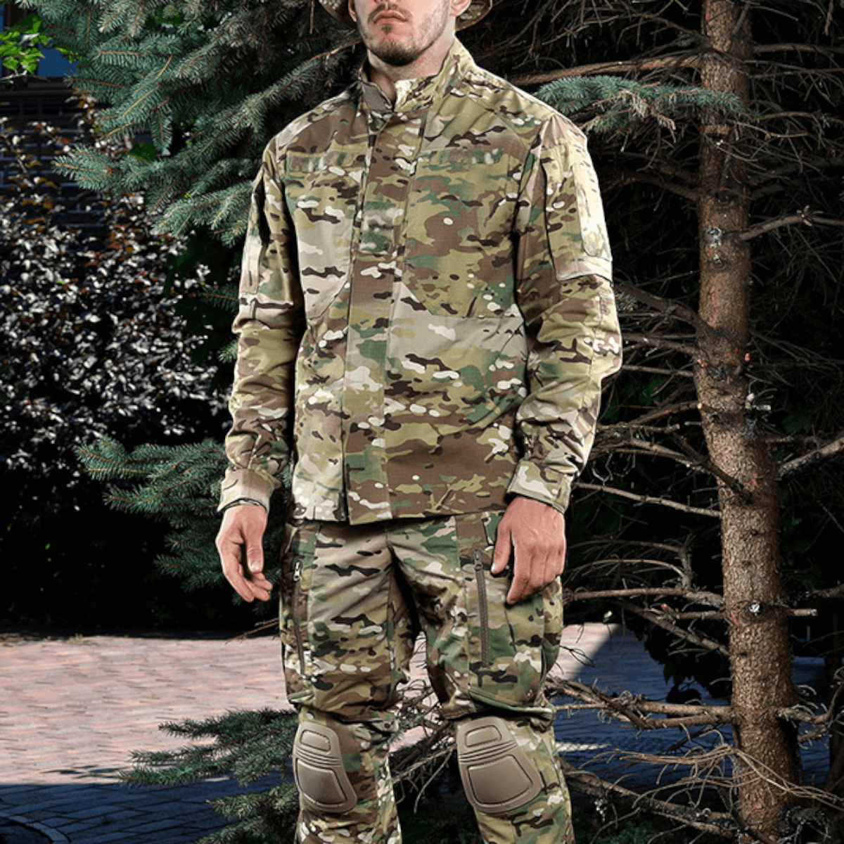 Mand i camouflageuniform står blandt træer.