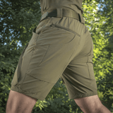 M-Tac Shorts Rubicon Flex mørkegrøn, med cargo-lommer og 4-way stretch til sommers brug, set bagfra i naturmiljø.